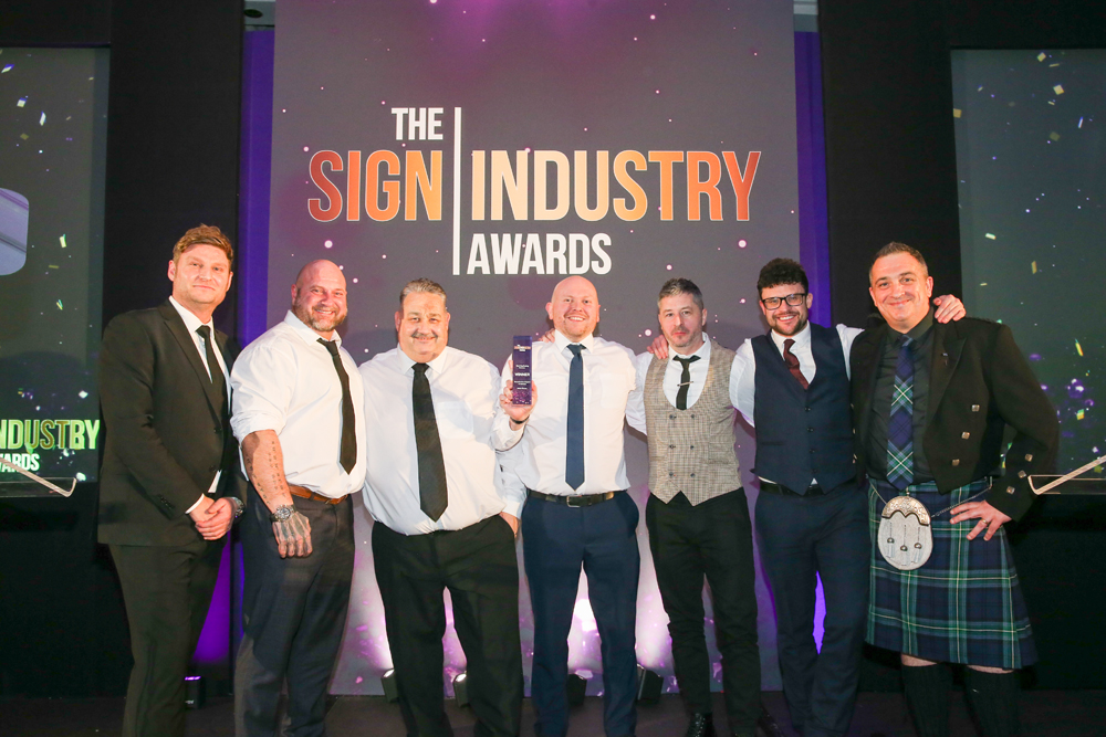 Astra Group team (seven men of varying ages) looking delighted to be collecting Wayfinding Scheme of the Year award at The Sign Industry Awards 2026.