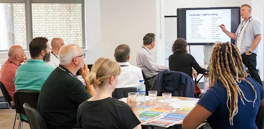 Group of people sitting in a training room avidly paying attention to the man leading the session.