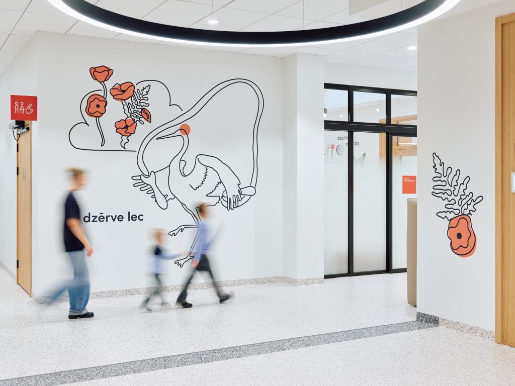 A bright, welcoming hallway brought to life with playful crane and floral illustrations in red and black. The terrazzo floor and clean white walls create a calm backdrop as a family walks through the space, adding a sense of movement and everyday life.