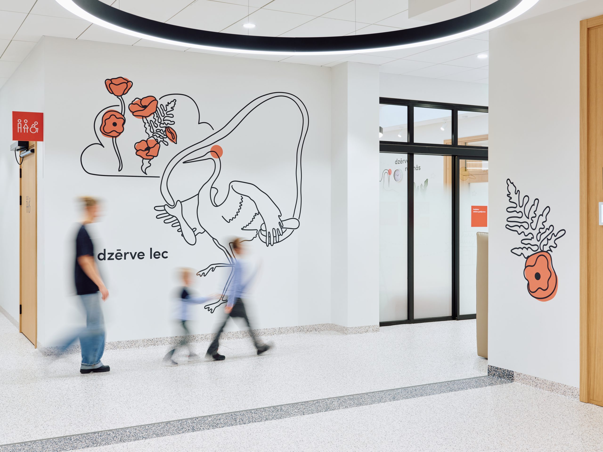 A bright, welcoming hallway brought to life with playful crane and floral illustrations in red and black. The terrazzo floor and clean white walls create a calm backdrop as a family walks through the space, adding a sense of movement and everyday life.