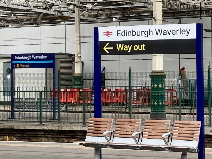 View of a platform at Edinburgh Waverley Station with wayfinding signage arrow showing the way out