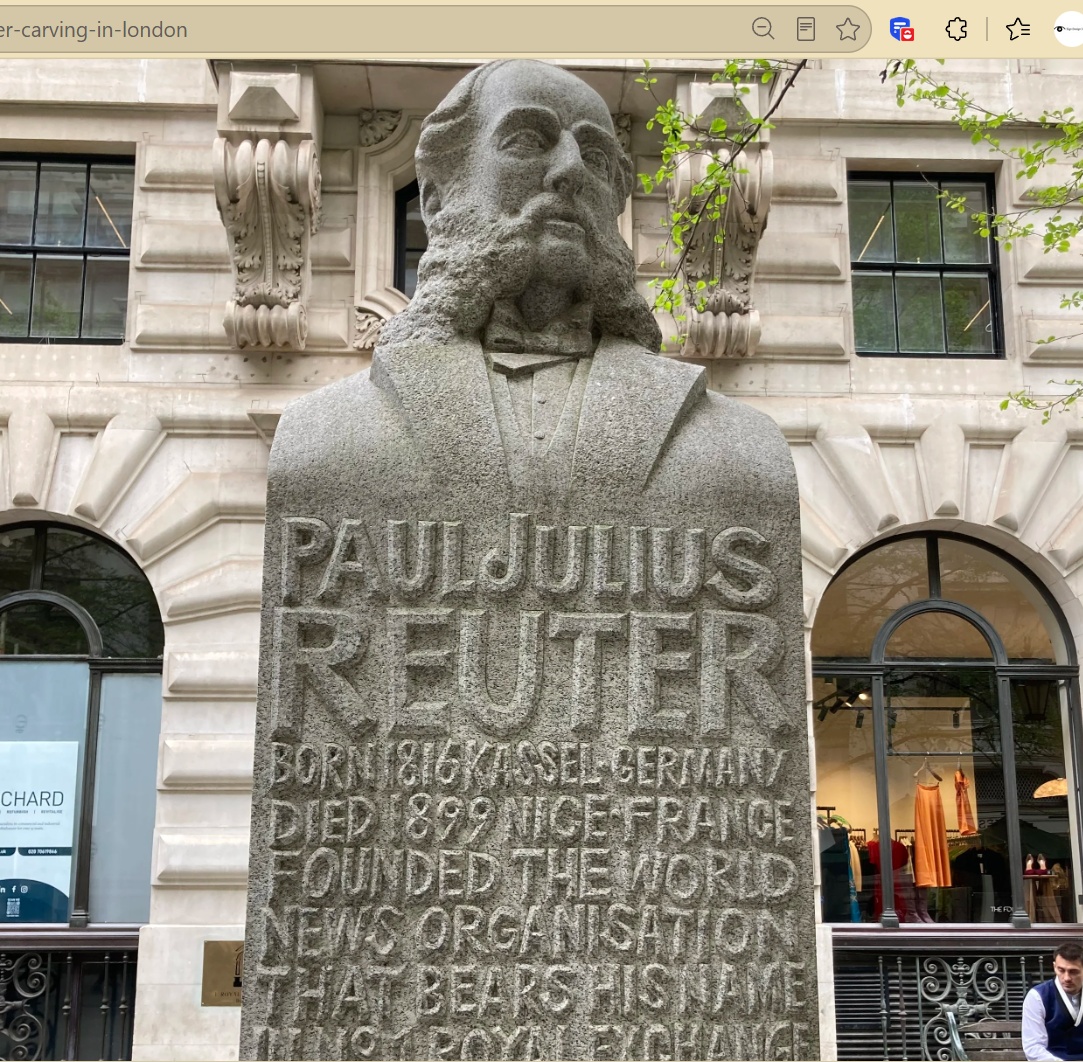 Stone bust of Paul Julius Reuter mounted on a plinth, with engraved text noting his birth in 1816, death in 1899, and his founding of the Reuters news organisation.