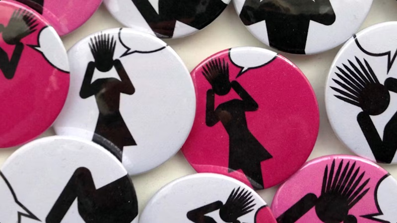 Close up of pink and white pin badges showing black silhoettes of women speaking out