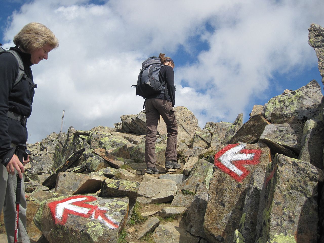 People climbing up craggy terrain, using wayfinding arrows drawn onto rocks to find the safest pathway