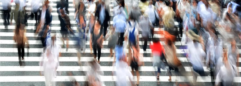 Blurred photo showing lots of people walking in both directions on a very wide urban Zebra crossing