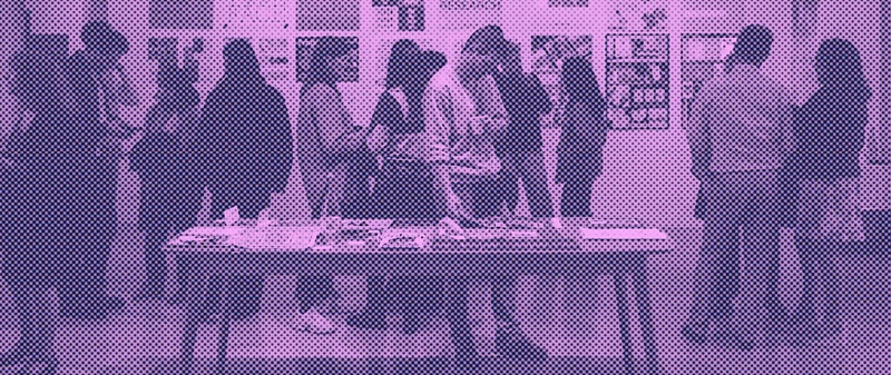 Photo (through a purple lens) of a mixed group of people standing around chatting and looking at exhibits at a previous Type Paris event.