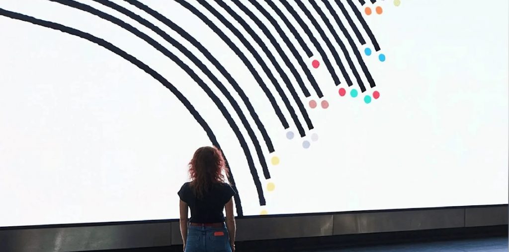 Woman standing looking at a very large white screen with data infographics on it