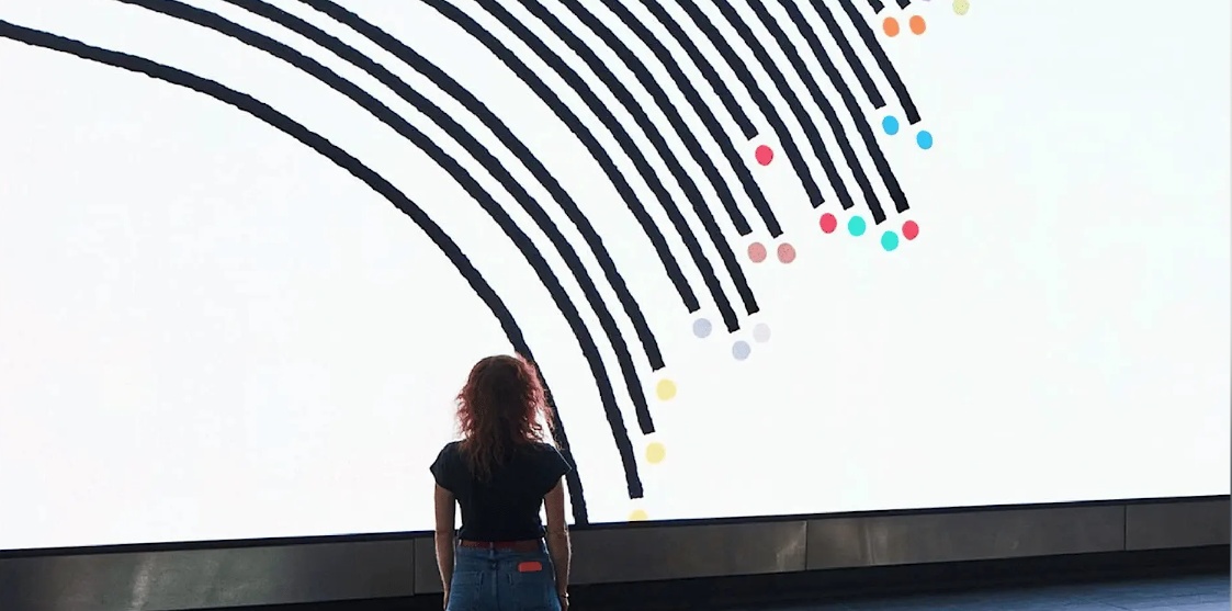 Woman standing looking at a very large white screen with data infographics on it