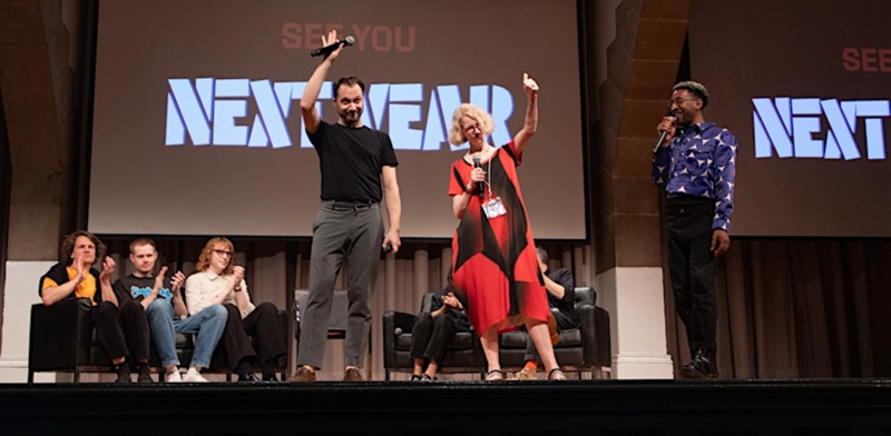 Photo of two speakers (Type Conference 2025) waving to the audience, microphones in hand as seated people (panel members? in the background on the stage clap in appreciation.